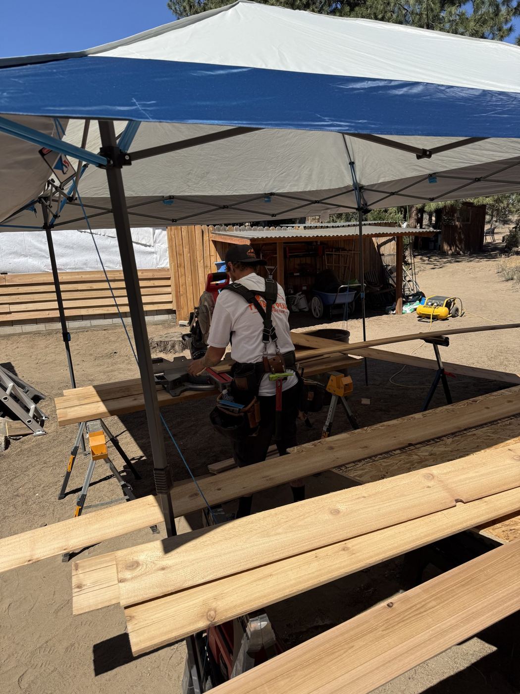 A Timber Peak crew member cutting cedar boards at a shaded cutting station on a job site